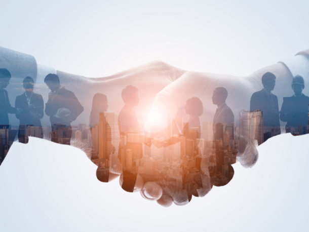 Two hands shaking with an overlay of business meeting and buildings in the background