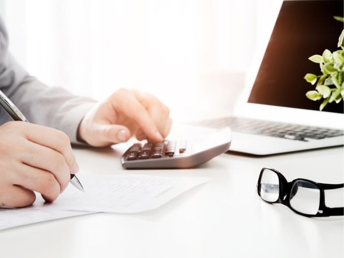 Energy worker on laptop and calculator on desk with glasses set on table