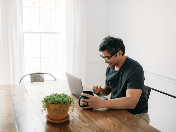 Home energy advisor working on laptop from his home on wooden table, plant sitting on the table